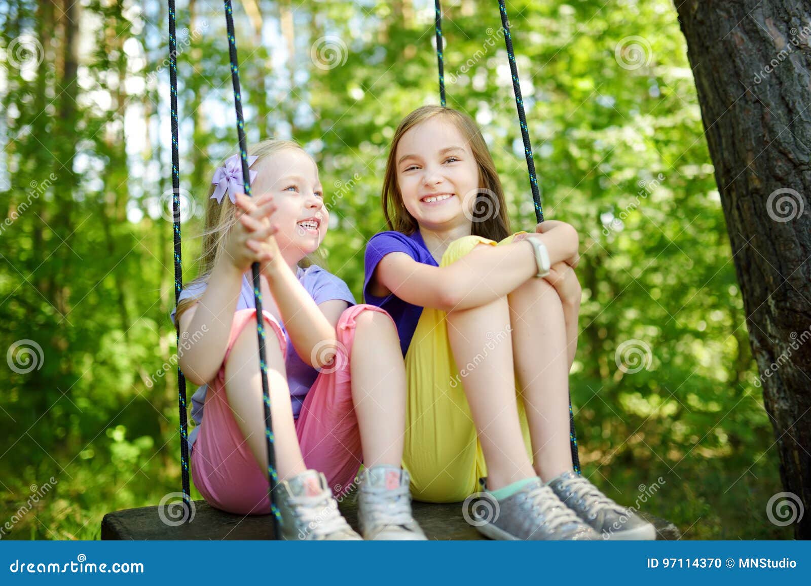 Two Cute Little Sisters Having Fun On A Swing Together In Beautiful