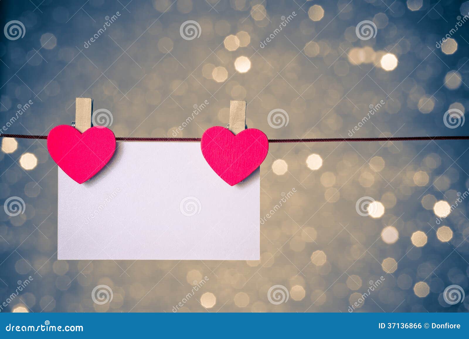 two decorative red hearts with greeting card hanging on blue and golden light bokeh background, concept of valentine day
