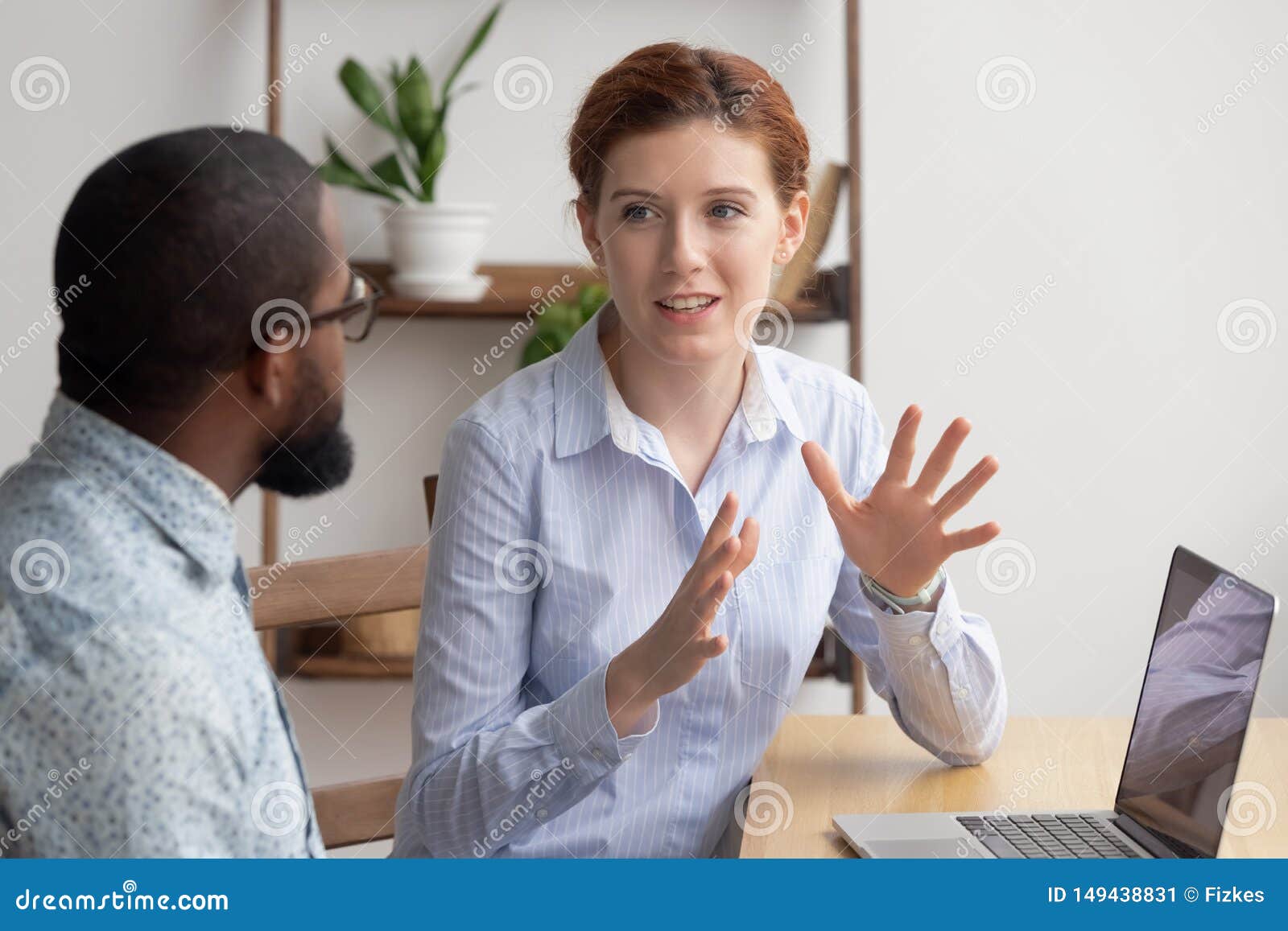 two diverse businesspeople chatting sitting behind laptop in office