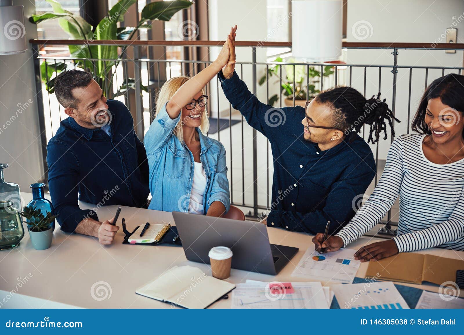 group of laughing coworkers high fiving during an office meeting