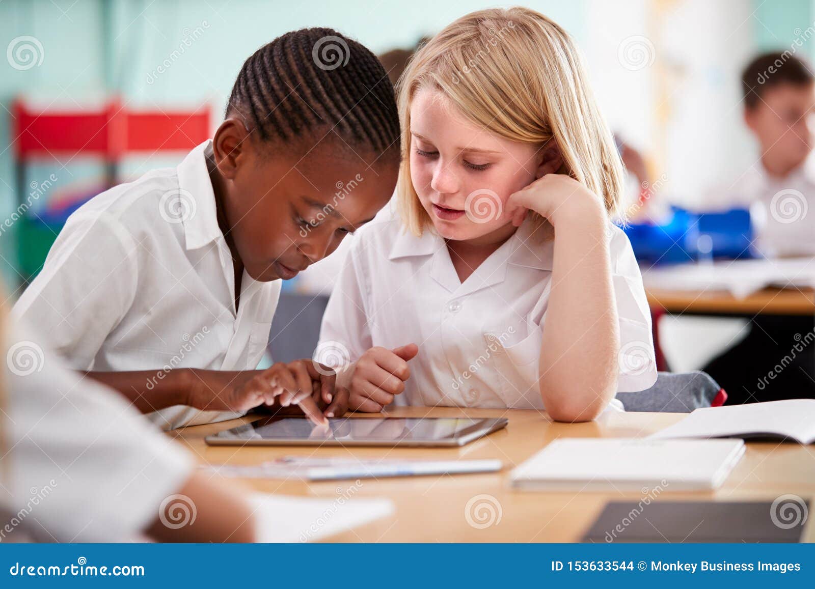 two ary school pupils wearing uniform using digital tablet at desk