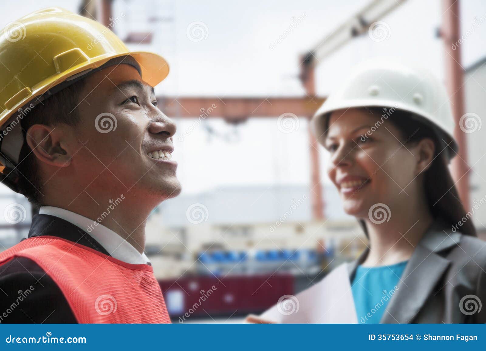 two engineers smiling in protective workwear outside in a shipping yard