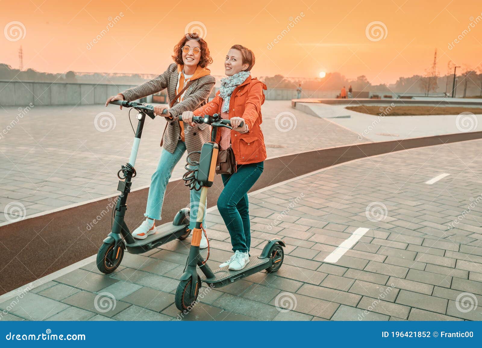 female friends ride modern rented electric scooters through the streets of the city. transport and lifestyle and friendships
