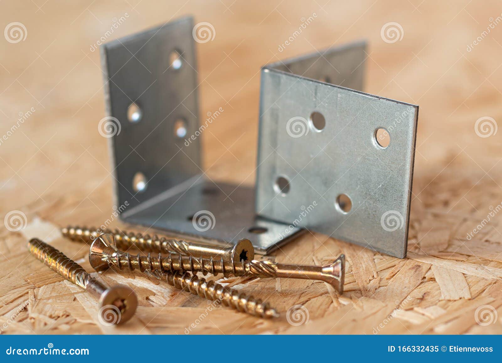 two galvanized angle brackets and self drilling screws lying on chip board. blurred background