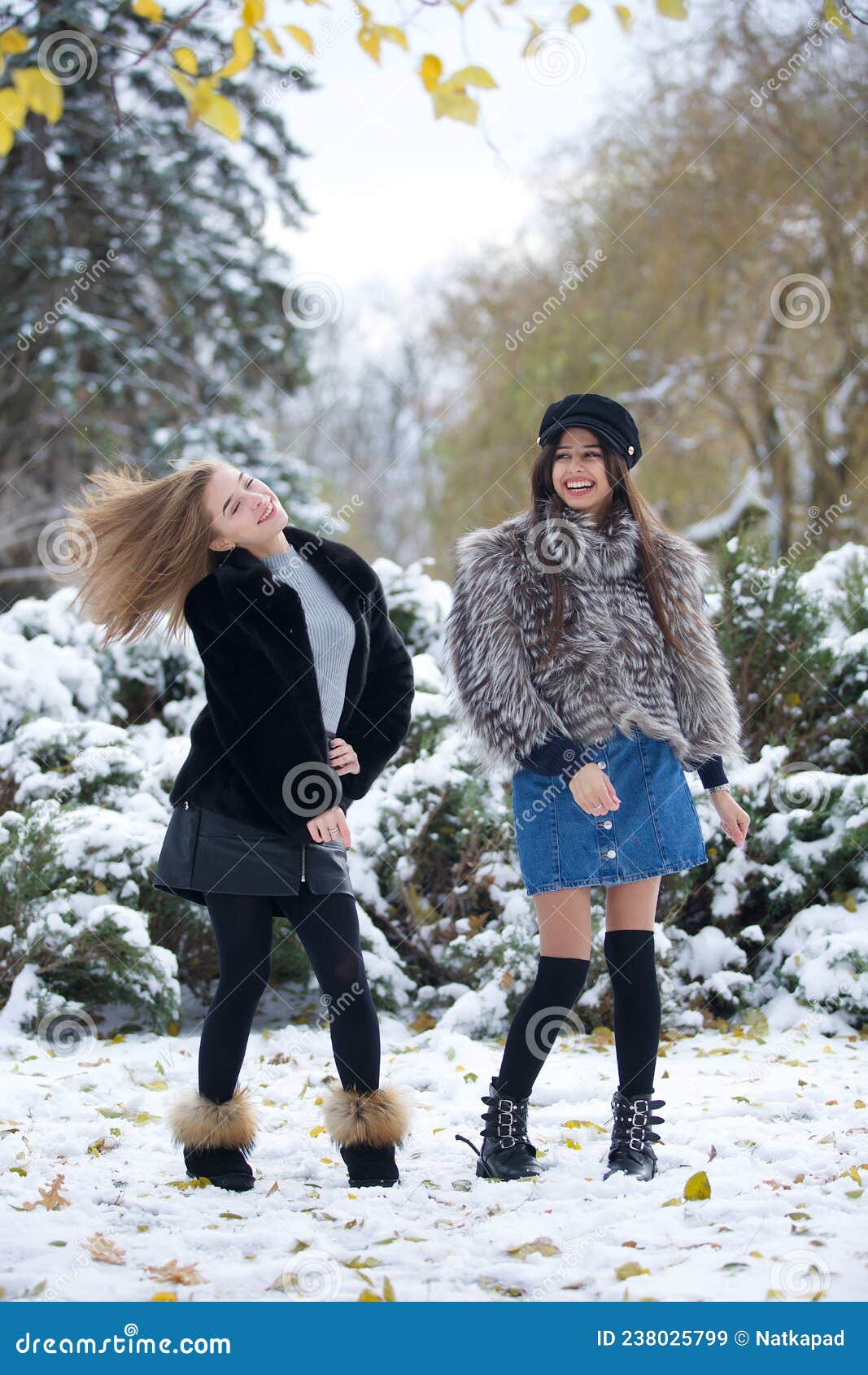 Two Girls in Fashionable Winter Clothes Stand Against the