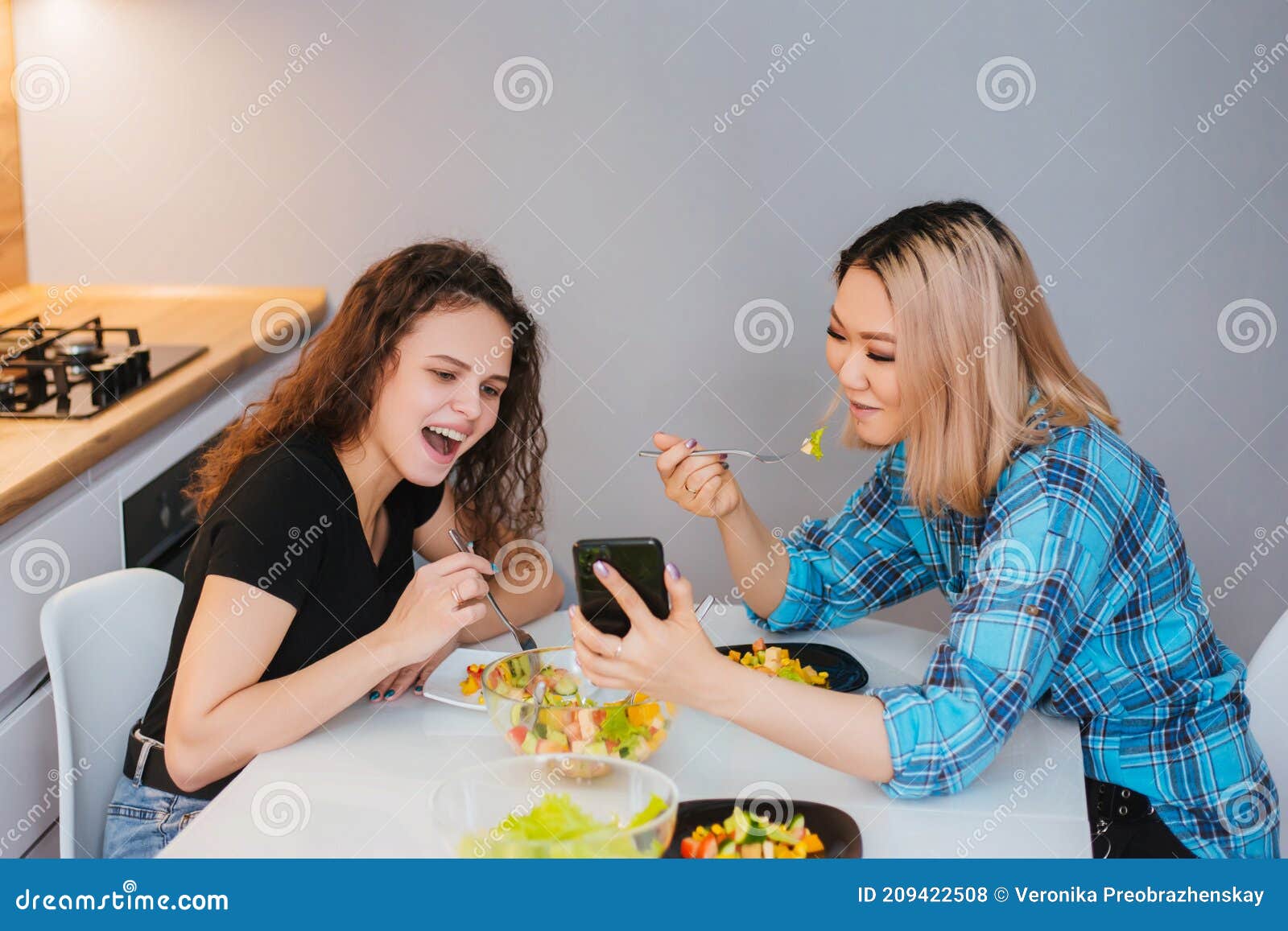 Two Girls are Sitting at the Kitchen Table, Eating Diet Salad and ...