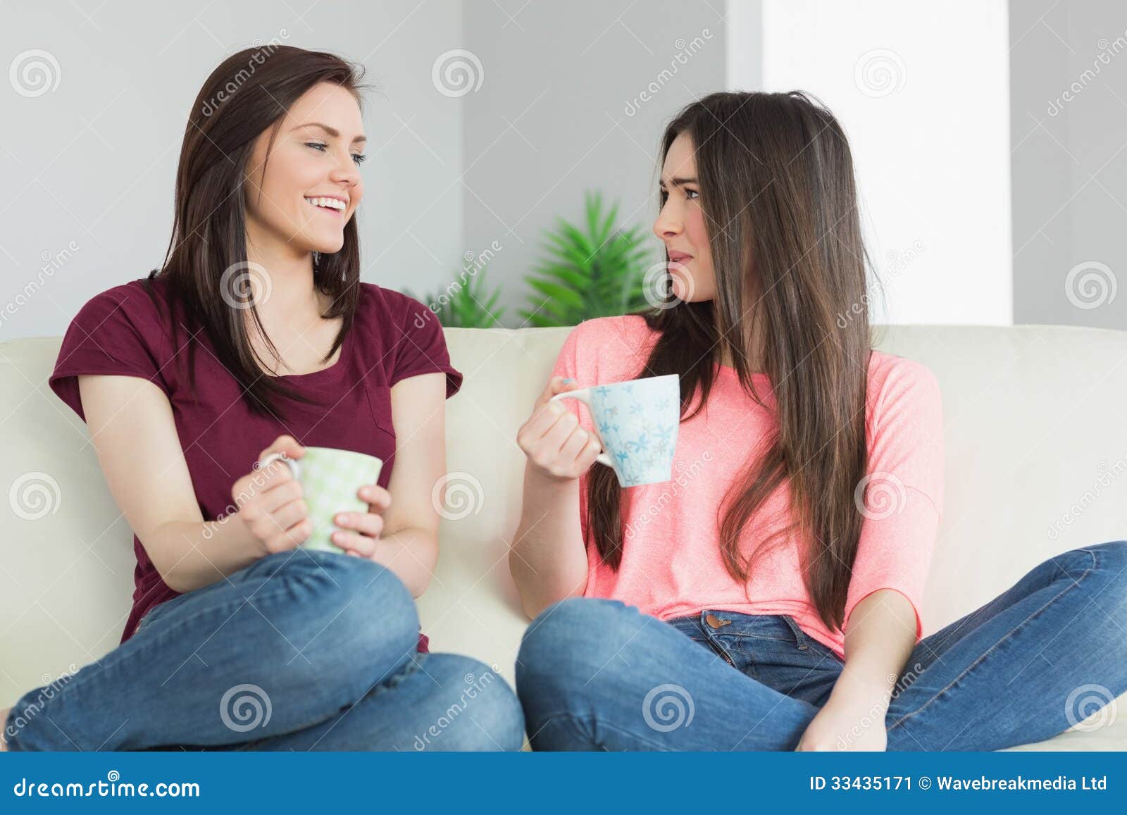 Two Girls Sitting On A Sofa Looking Each Other And Drinking A Be Stock Image Image Of Cheerful