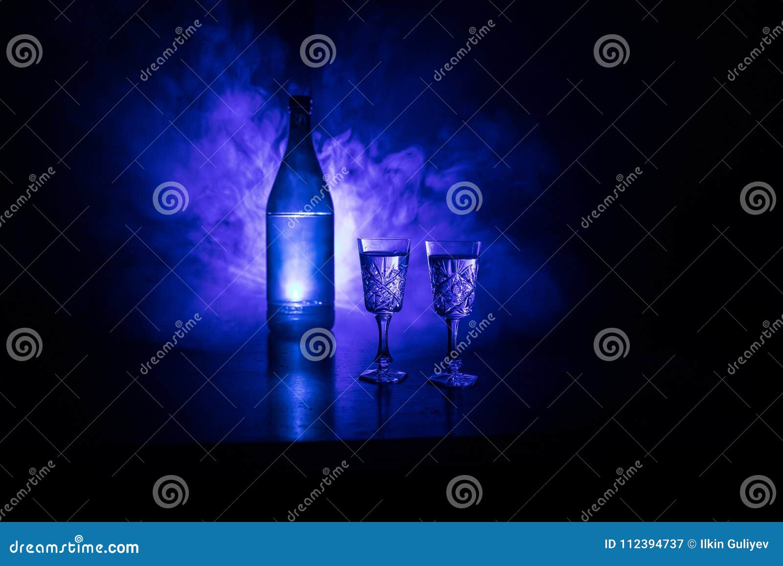 two glasses of vodka with bottle on dark foggy club style background with glowing lights (laser, stobe) multi colored. club drinks