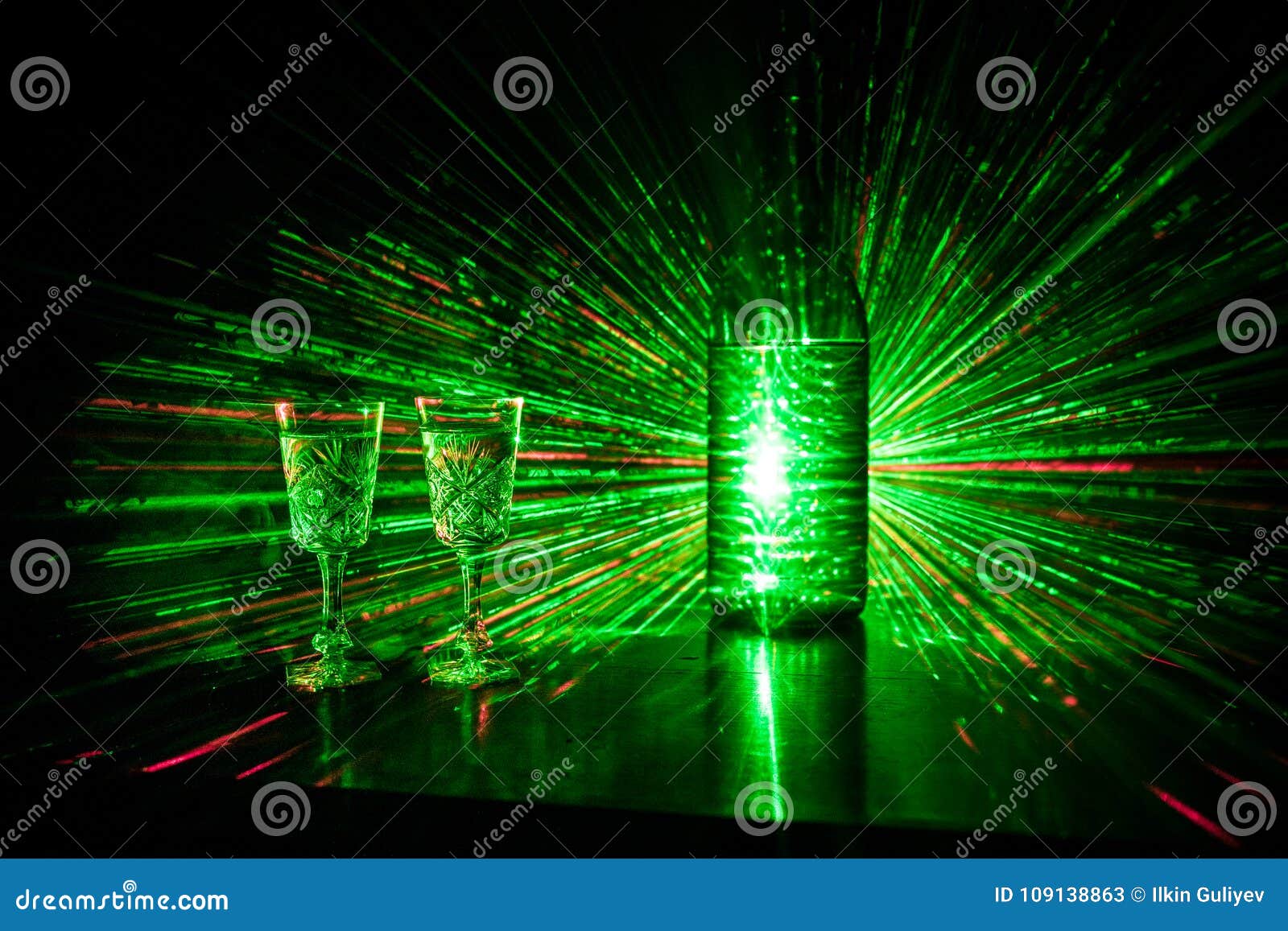 two glasses of vodka with bottle on dark foggy club style background with glowing lights (laser, stobe) multi colored. club drinks