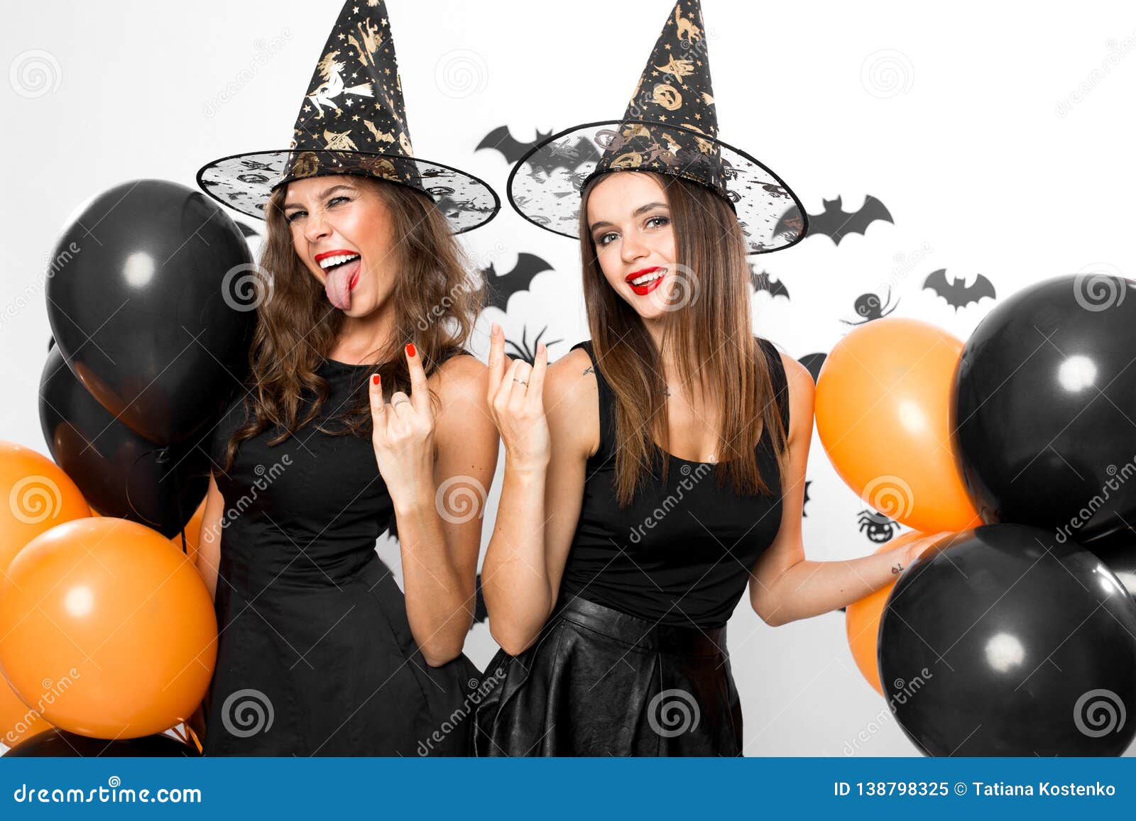 Two Gorgeous Women in Black Dresses and Witch Hats Make Grimace and ...