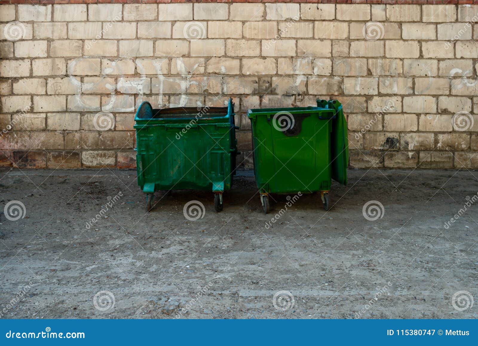 Two Green Trash Dumpsters in Front of White Brick Wall Front View with