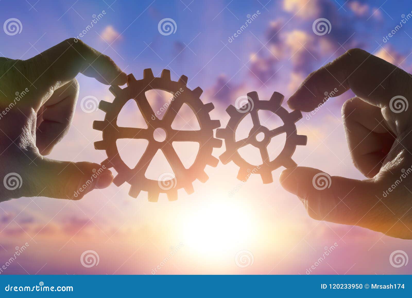 two hands connect the gears, the details of the puzzle. against the sky with sunset.