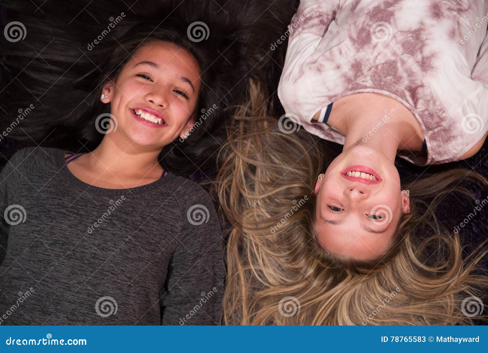 Two happy kids looking up from floor. Two girls laying down and looking up at camera with big smiles