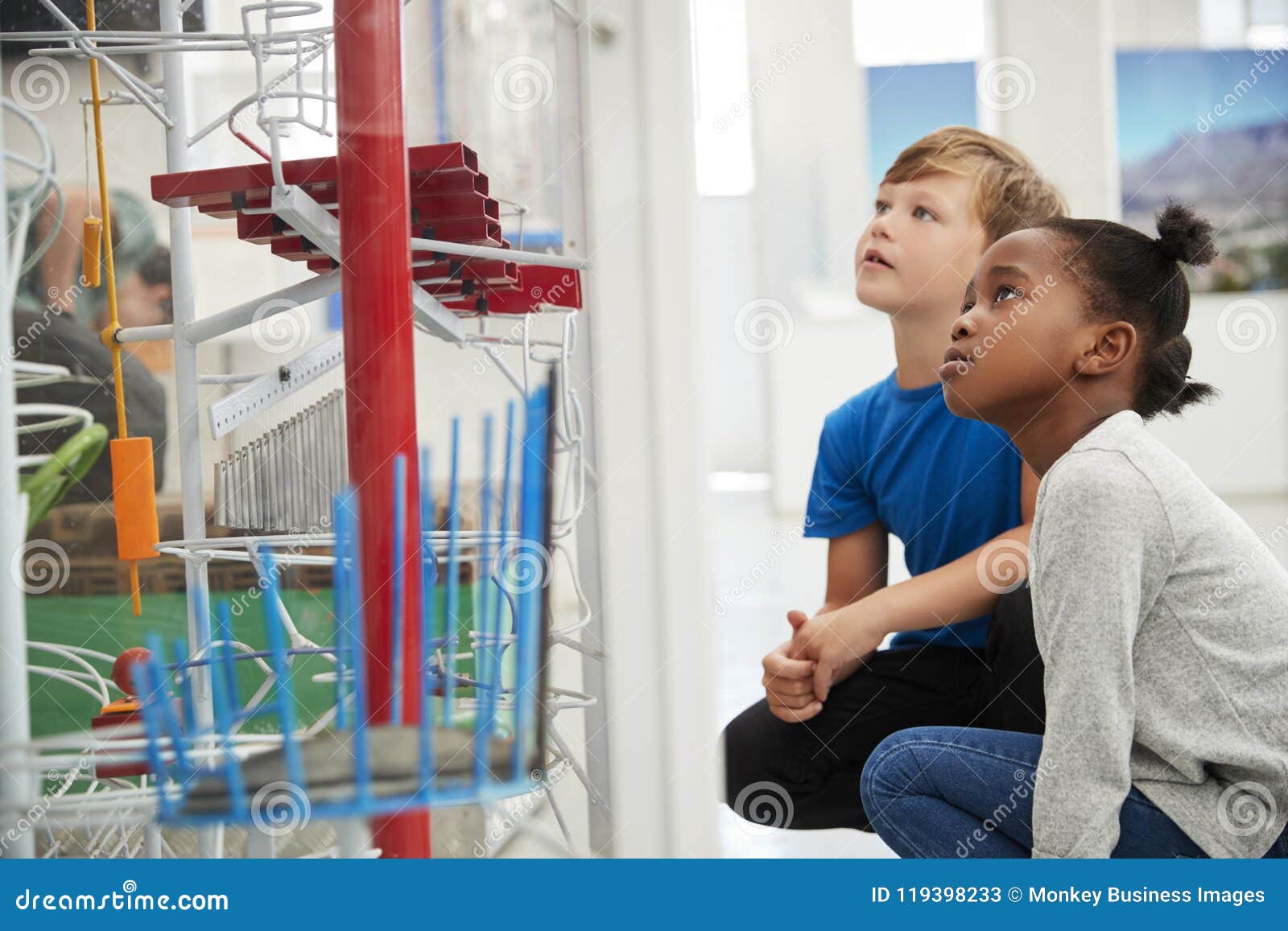 two kids kneeling and looking at a science exhibit