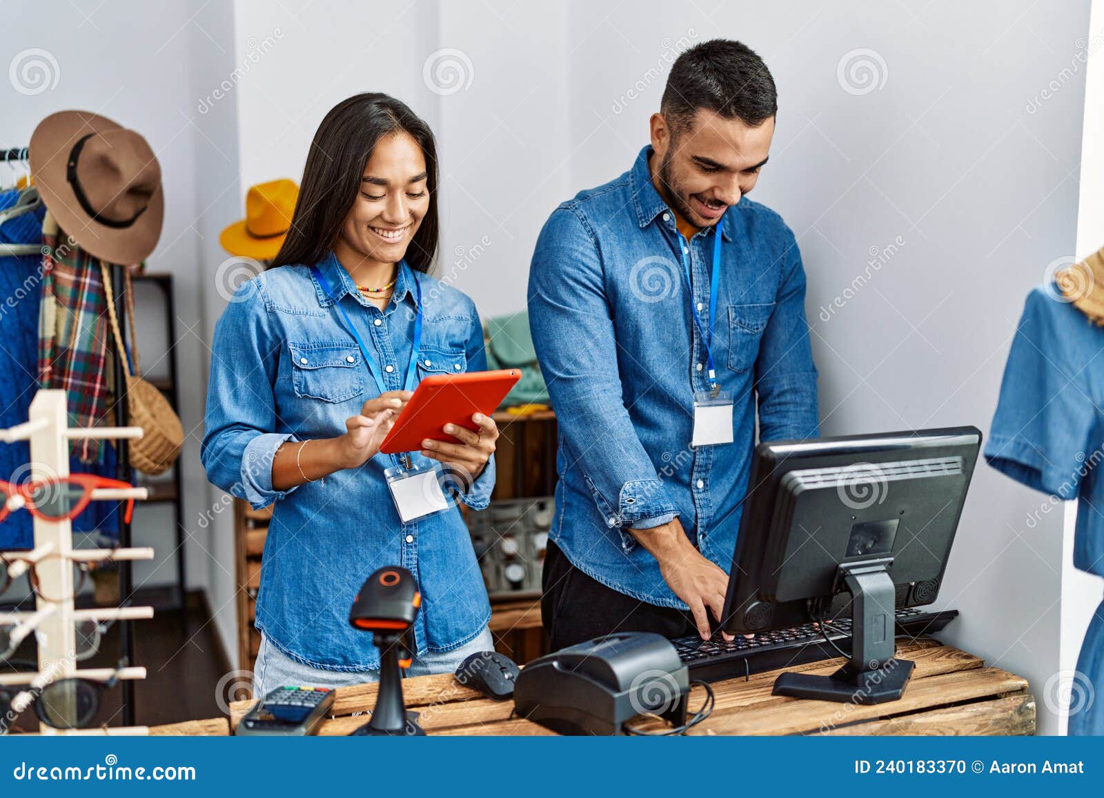 Two Latin Shopkeepers Using Touchpad Working at Clothing Store Stock
