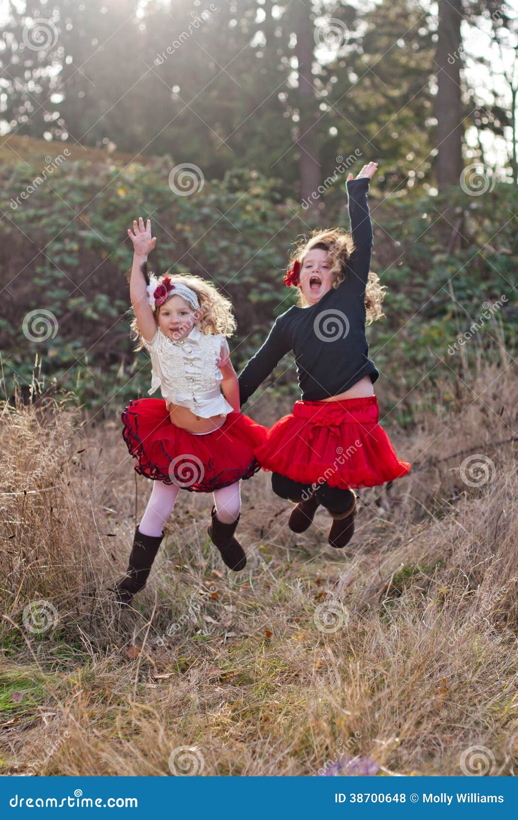 Two little girls dancing outdoors. Two charming little girls dancing wildly in the field wearing retro clothes, one with a black jumper and frilly red skirt and the other a white blouse with a frilly red skirt.