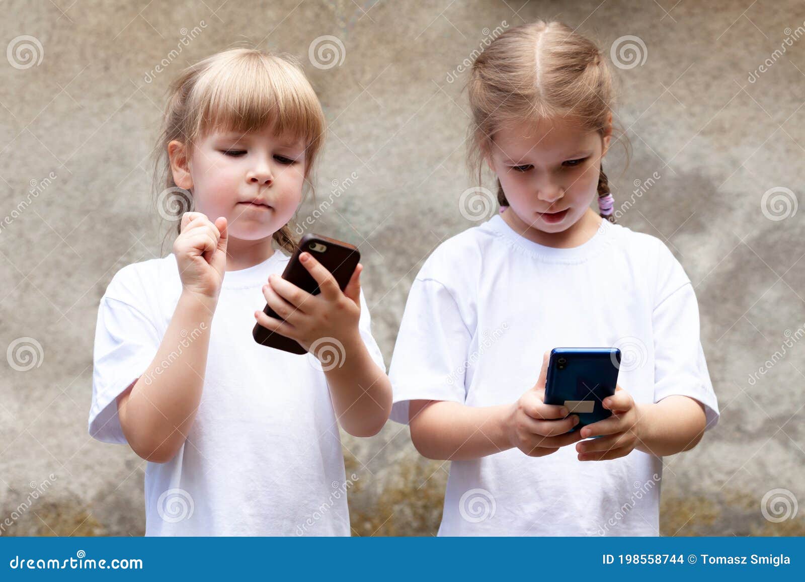 two little girls, sisters using modern smartphones, young children holding their mobile phones, playing around. new generation