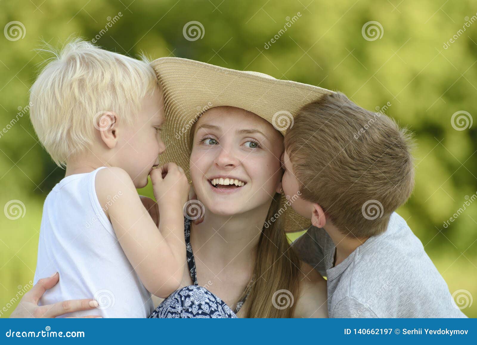 Two Little Sons Hug The Mother And Kiss On The Cheek Against The