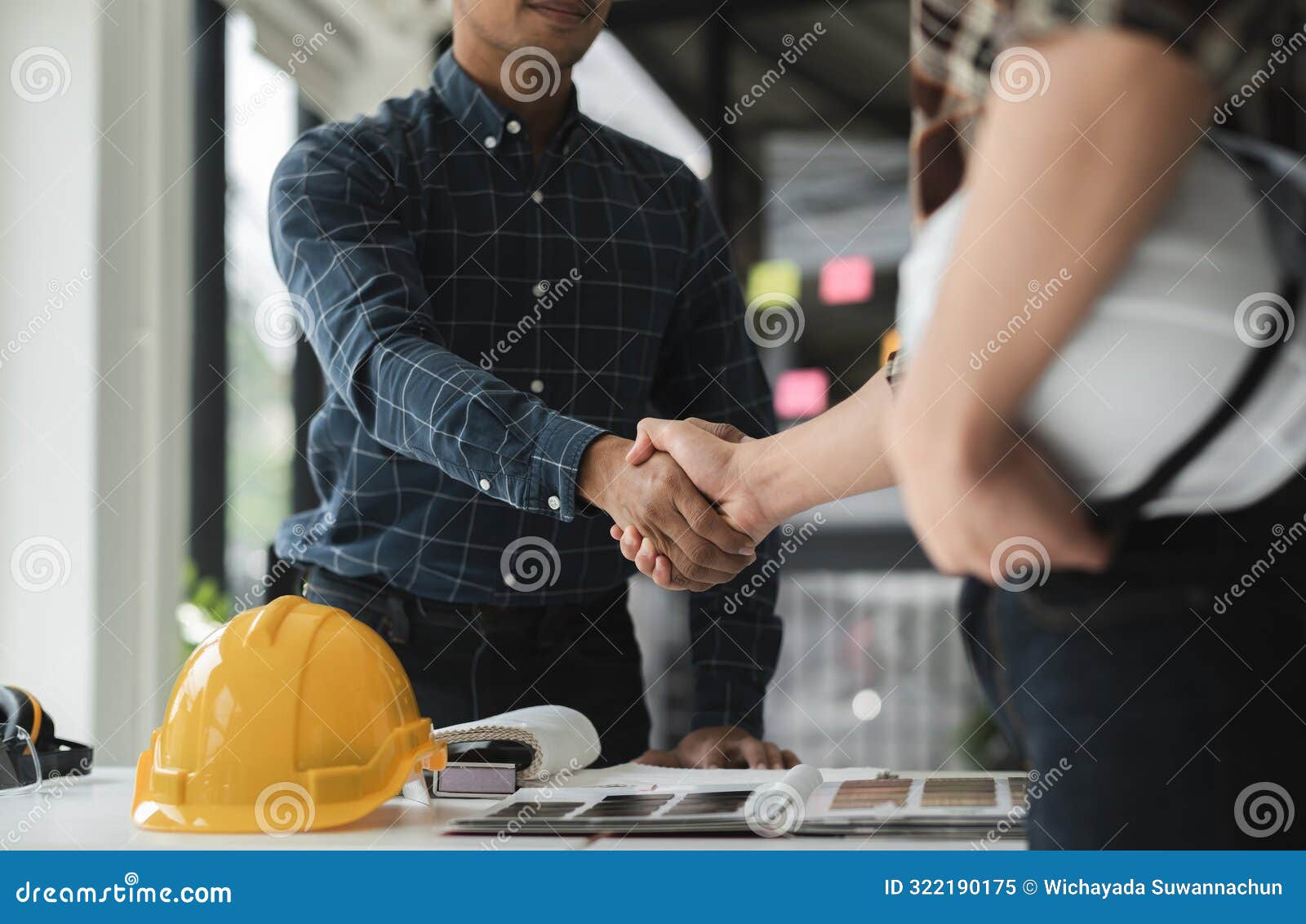 two male engineers shaking hands in modern office environment, collaborating on construction project with safety helmet