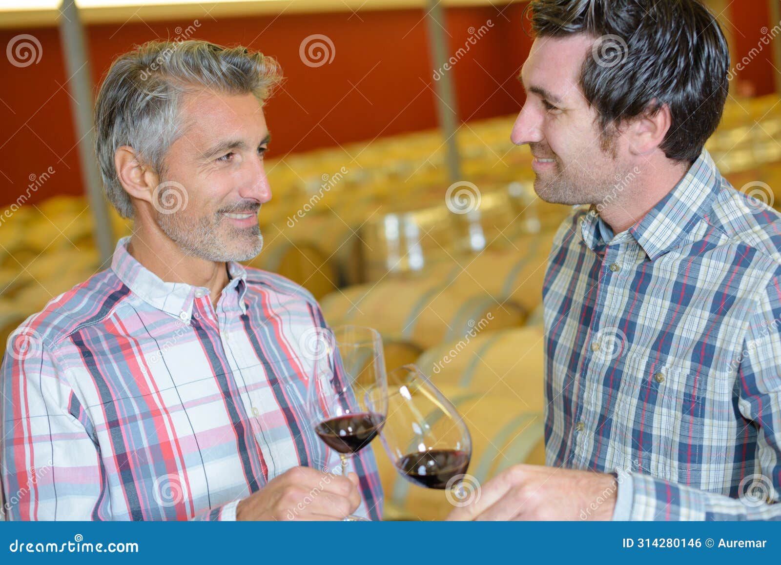two male winemakers tasting wine in glass in winery cellar