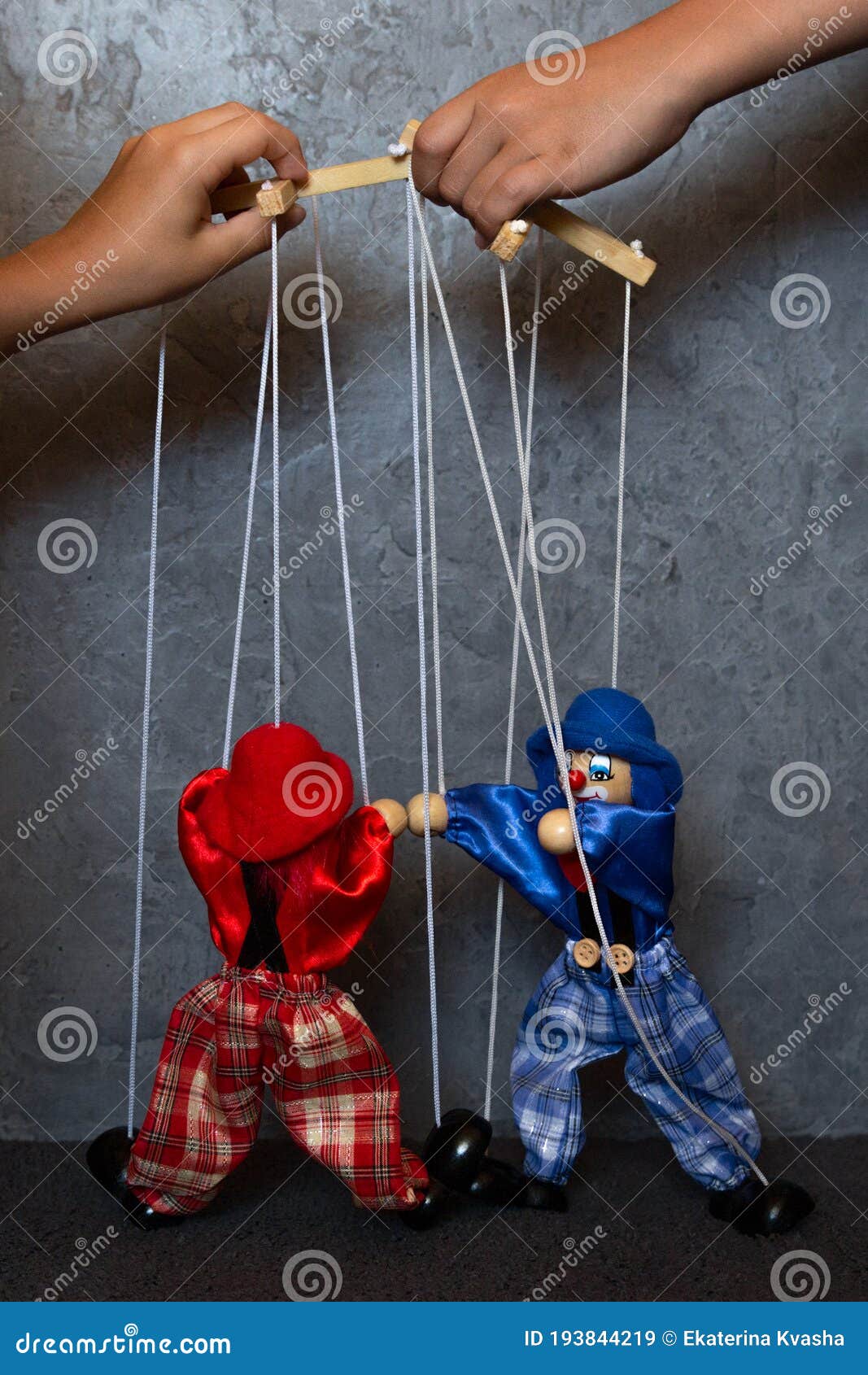 two marionette dolls on thin threads, controlled by hands, on a gray background