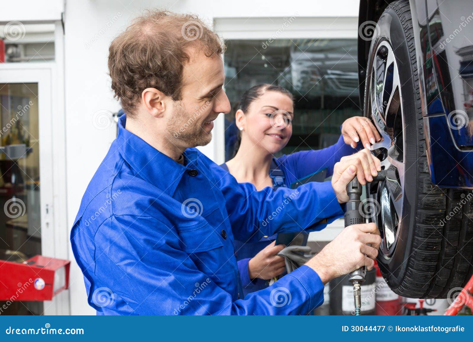 Car Mechanics Changing Wheel Working on Hydraulic Lift Stock Image