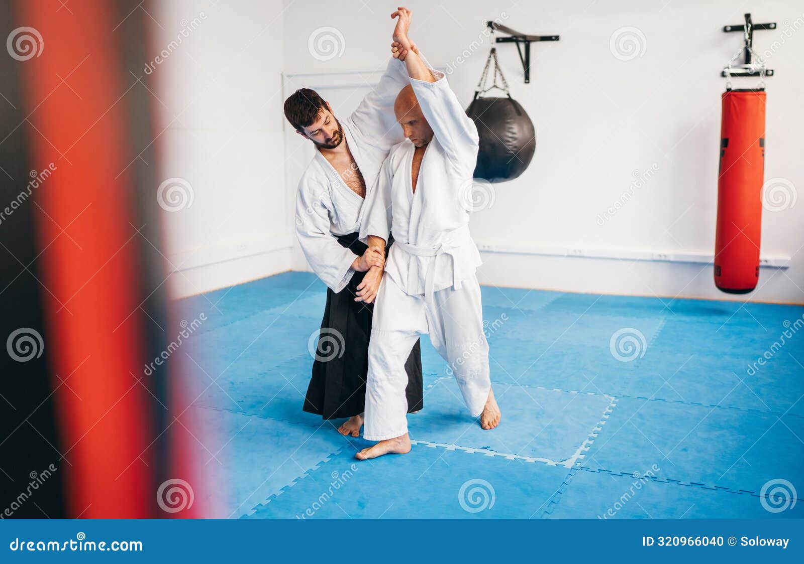 two men are practicing aikido in dojo wearing traditional white kimono and hakama .one man executes technique from ushiro ryote