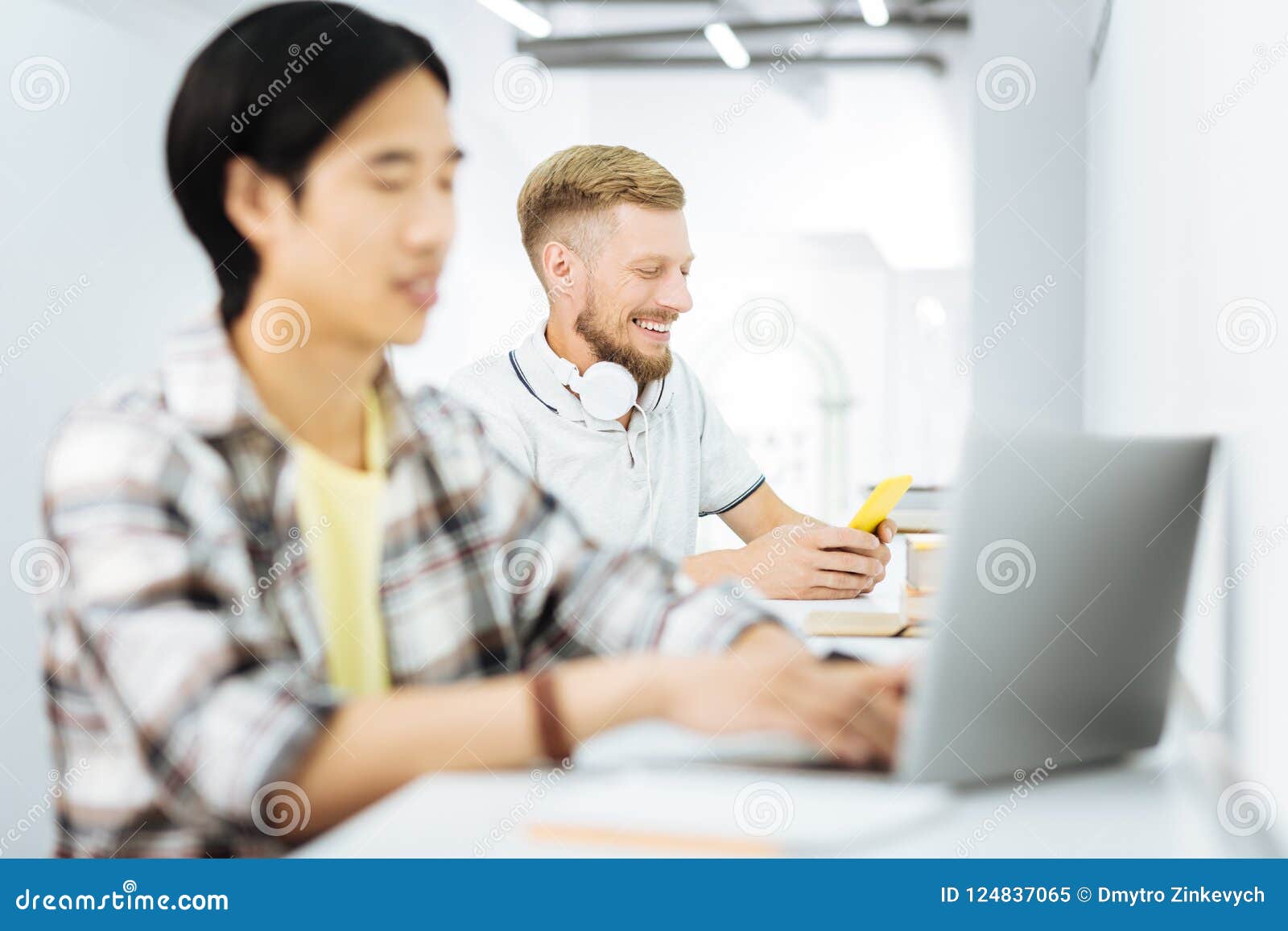 Two Men Sitting At The Desk And Being Occupied With Their Devices