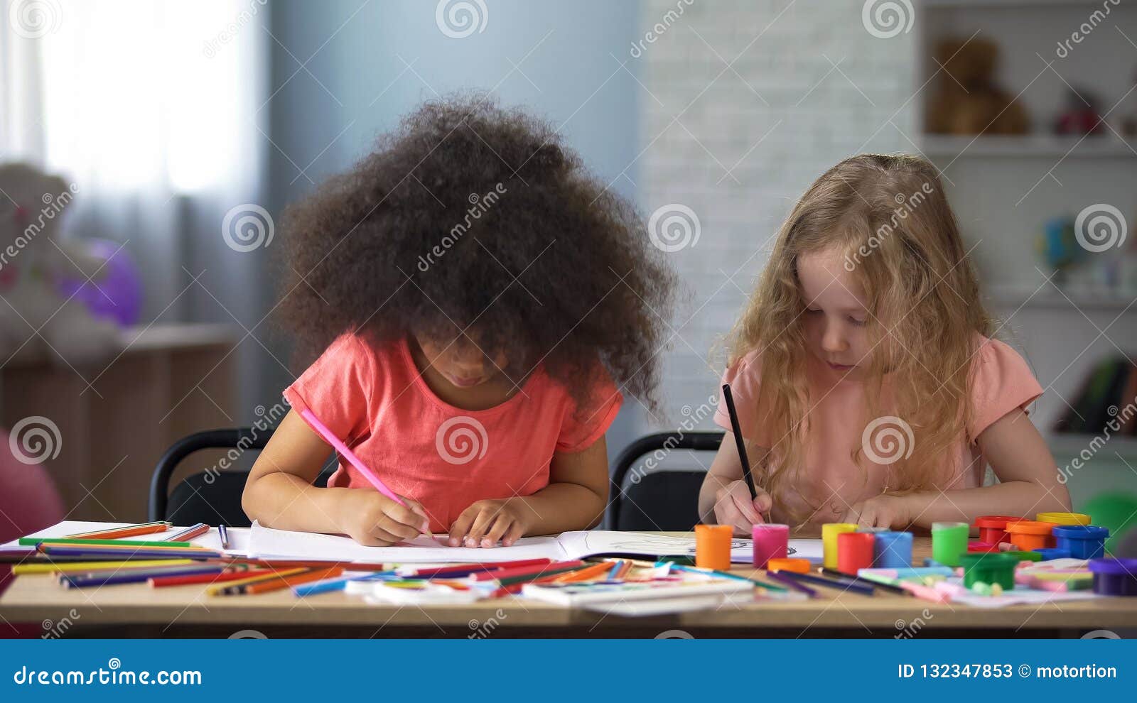 two multi-racial girls drawing with colorful pencils in early education center