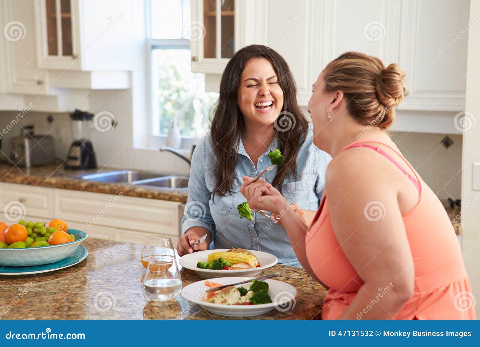 Two Overweight Women On Diet Eating Healthy Meal In Kitchen