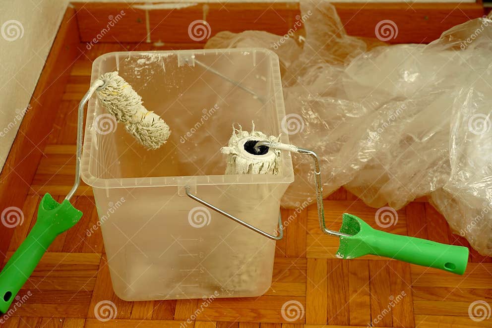 Two Paint Rollers in a Container on the Floor. the Paint is Dripping