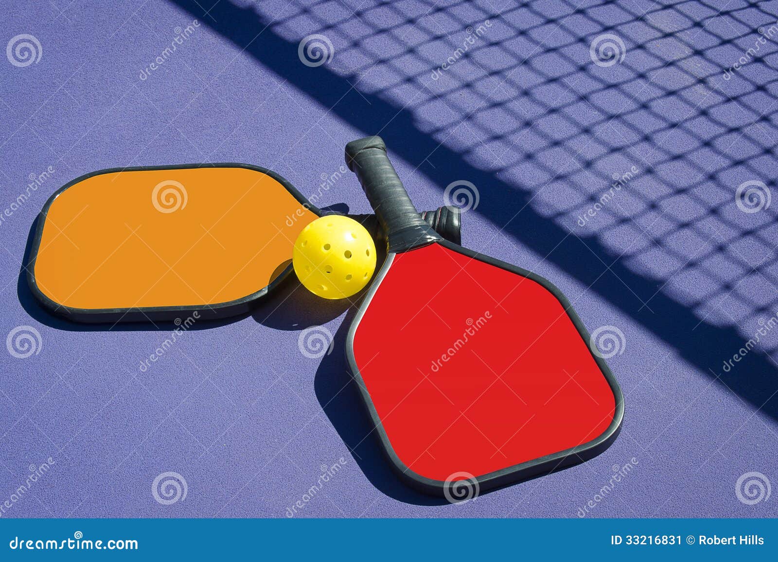 two pickleball paddles and a pickleball on court with net shadow