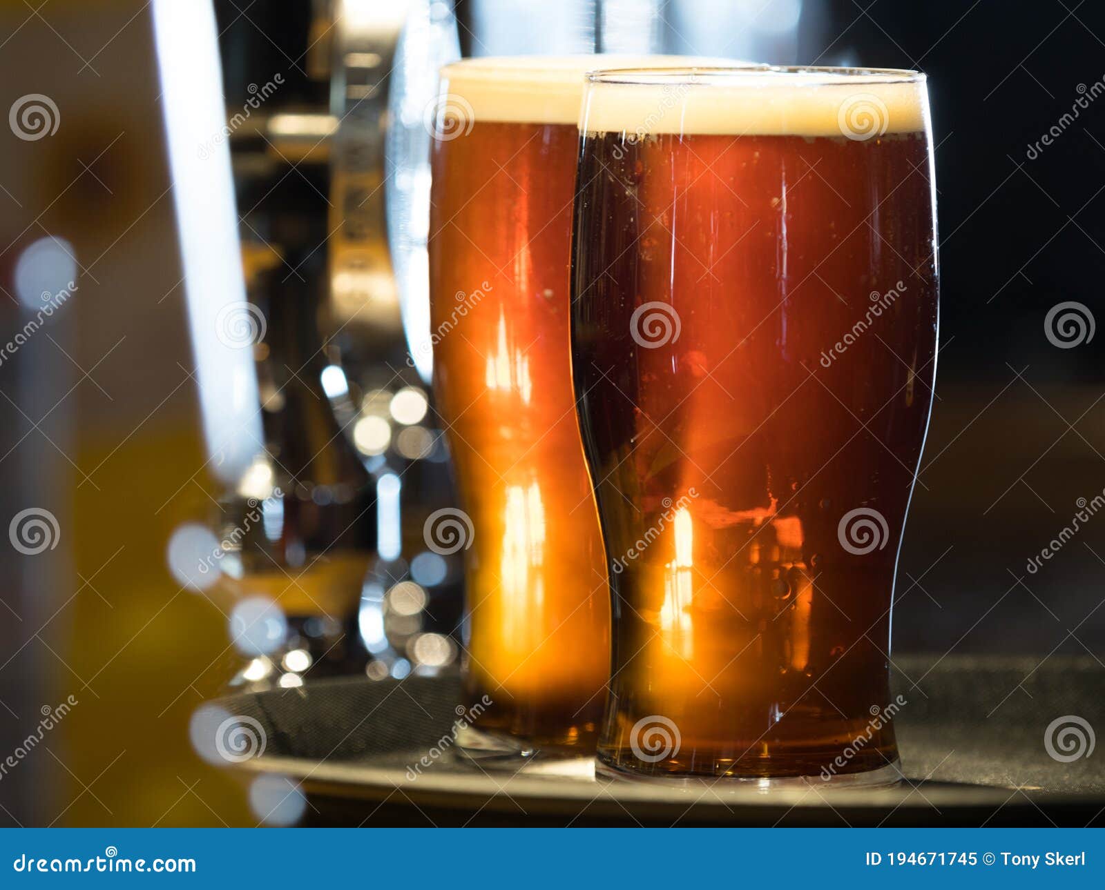 two pints of dark beer sit on a bar top