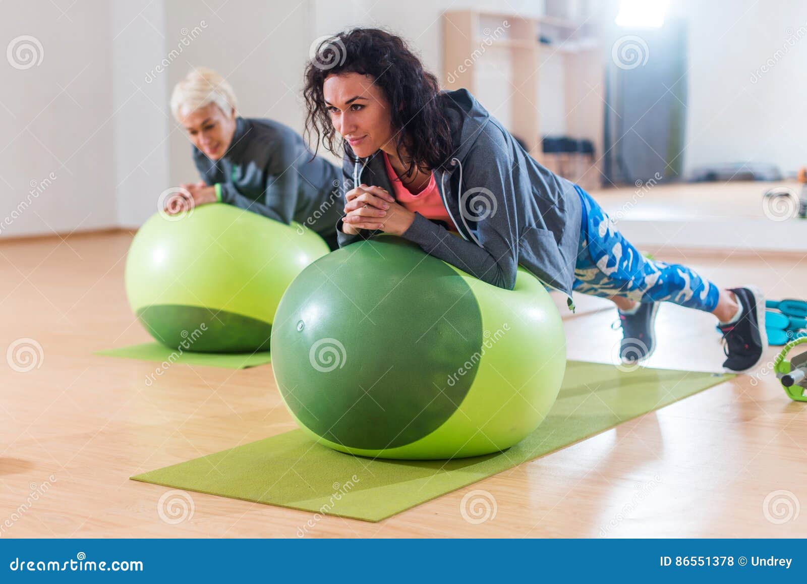 two positive women doing plank exercise lying on balance ball in gym