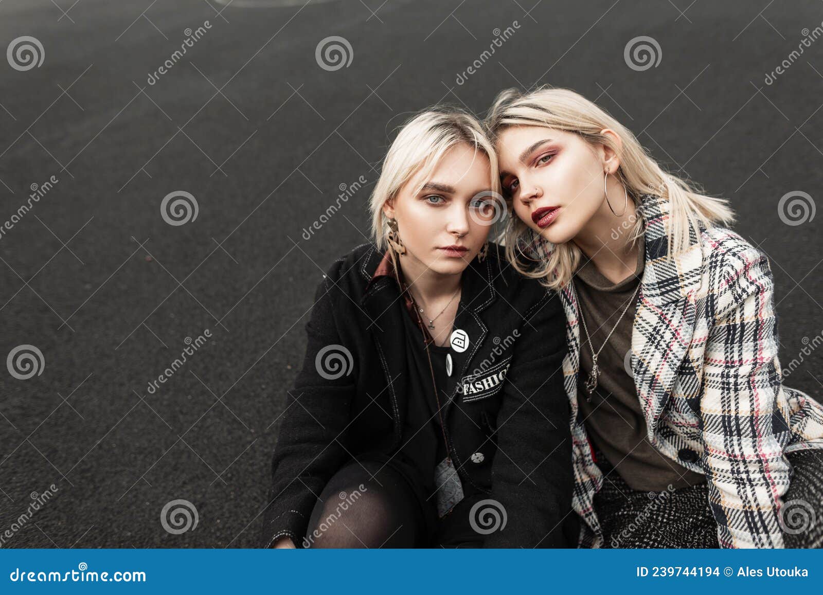 two pretty young girlfriend blondes in stylish clothes with sexy lips relaxes on ashphalt outdoors. portrait urban fine modern