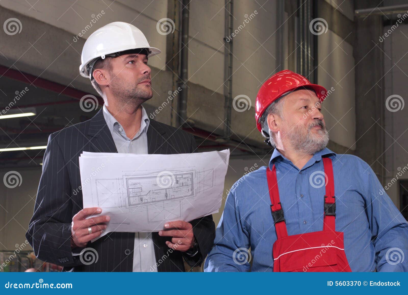 Two professionals with set of blueprints. Businessmen and older worker, wearing hardhats looking at a set of blueprints and discussing a construction project.