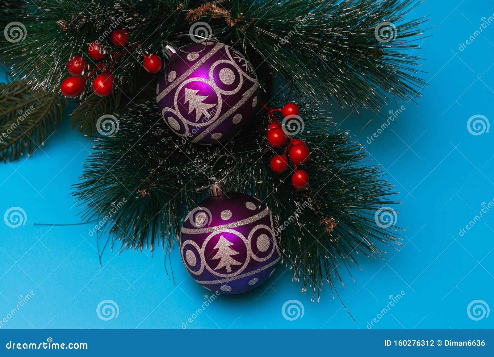 two purple festive balloons with the image of a christmas tree and snowflakes lie on artificial branches of a spruce, blue