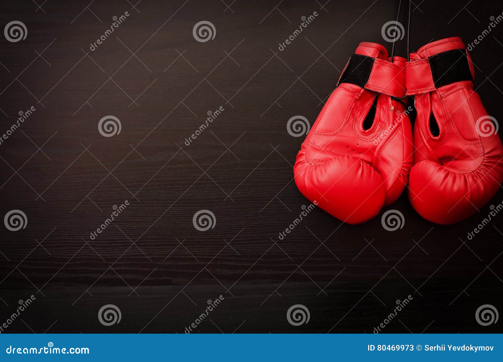 Two Red Boxing Gloves Hanging on a Black Background in the Corner of