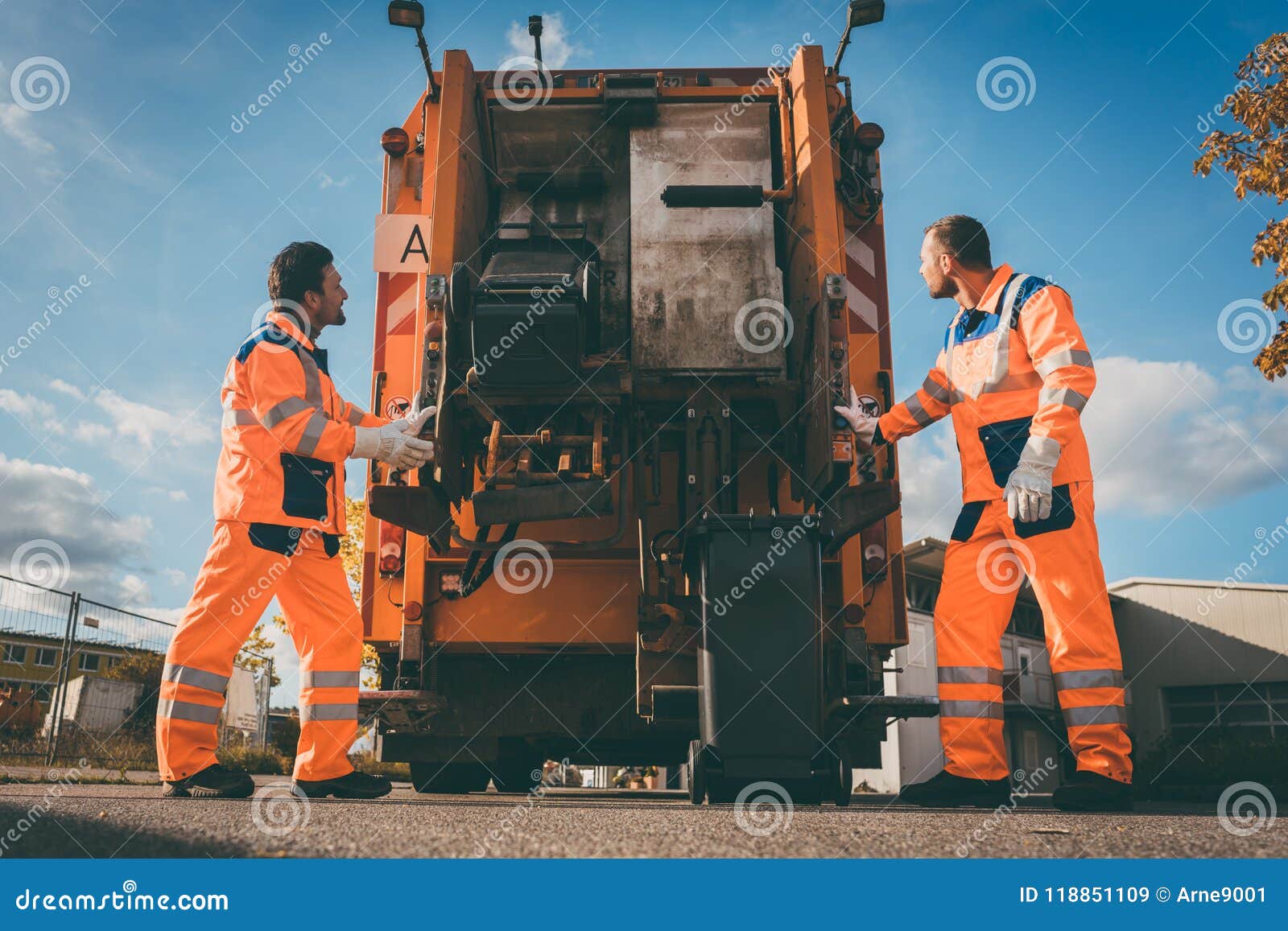 two refuse collection workers loading garbage into waste truck