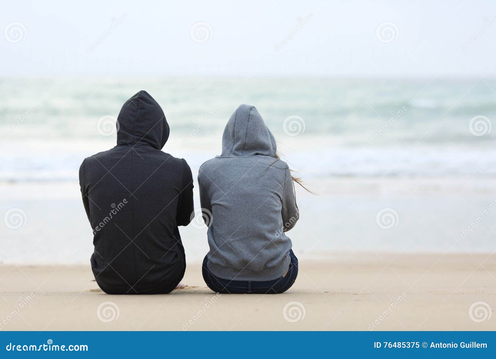 two sad teenagers sitting on the beach