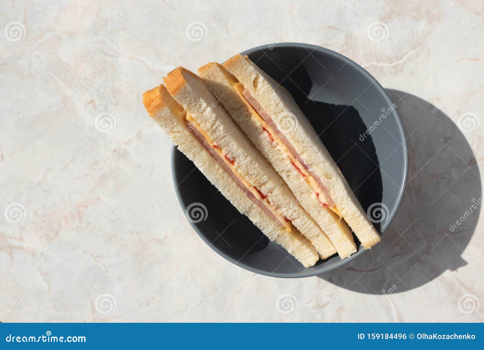 two sanwiches with ham, cheese and tomatoes in gray deep plate on light  marbled table