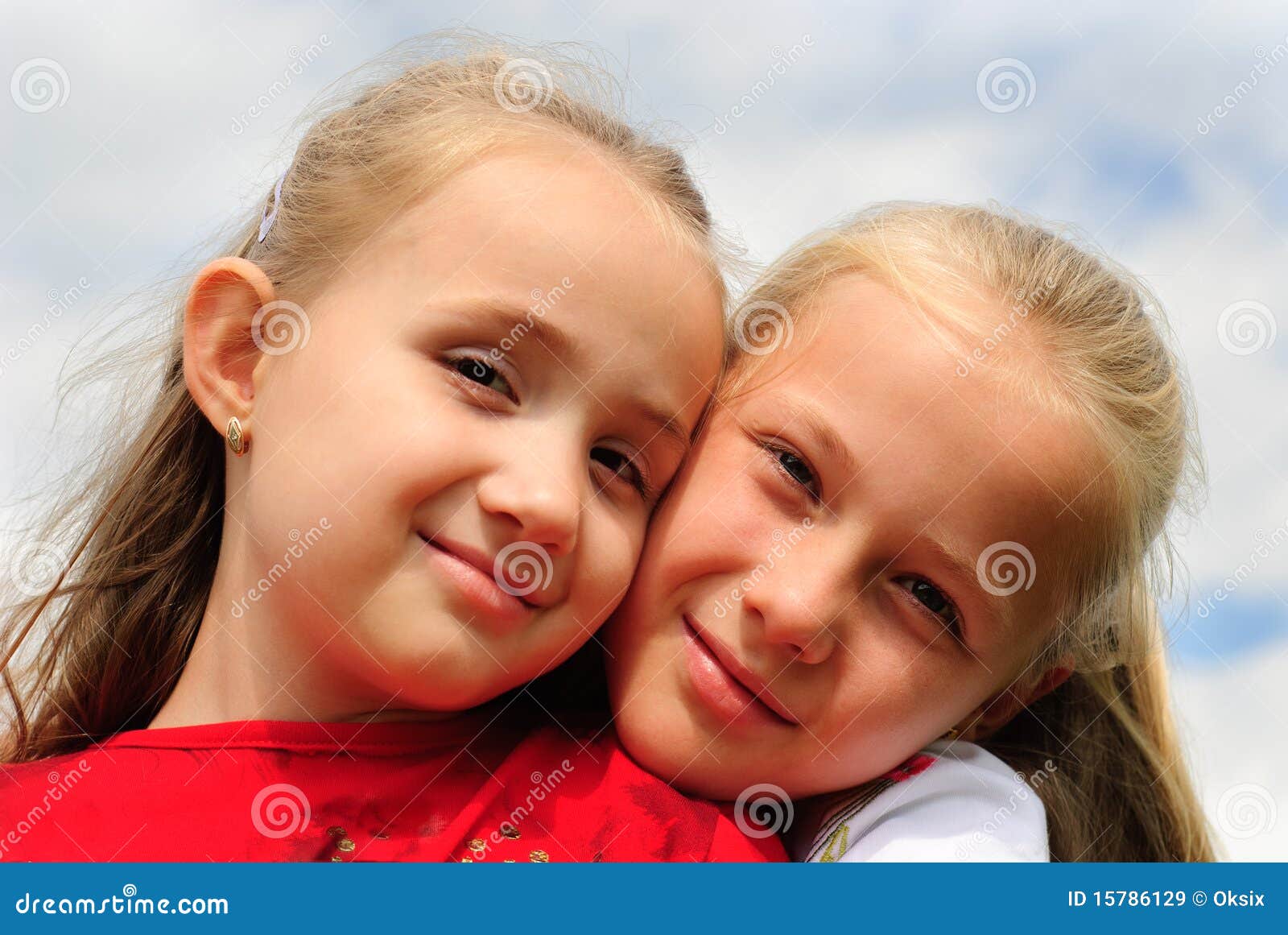 Two sisters hug one another outdoors, happy family. Close up faces.