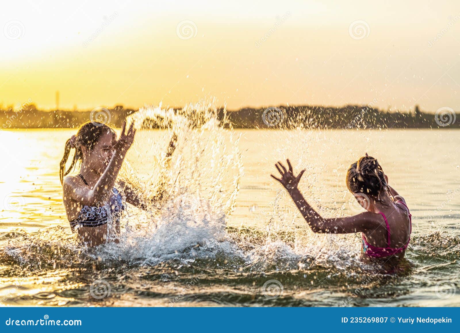 Two Sisters Splashing Water Playing In The Lake At Sunset Background