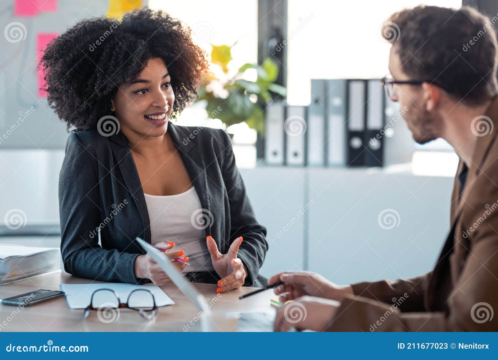 two smart multiethnic business people working together with laptop while talking about job news in the office