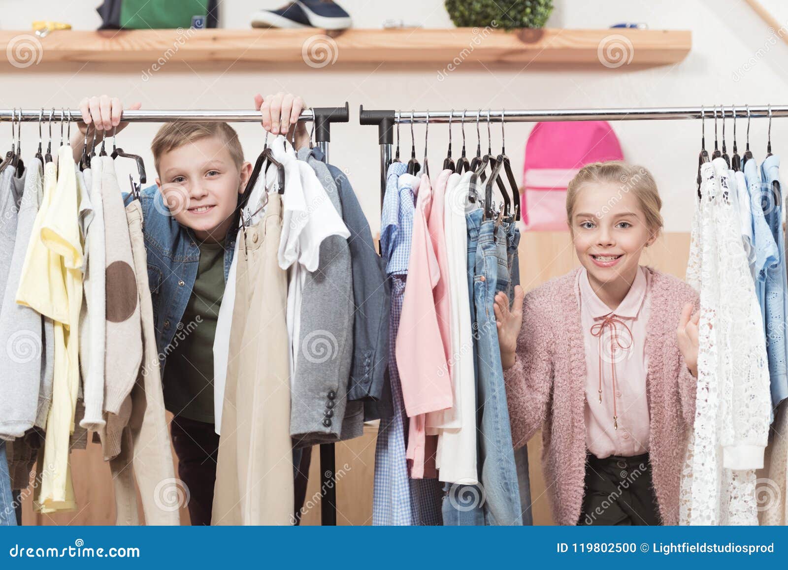 Two Smiling Kids Looking at Camera while Standing Under Cloth Hanger ...