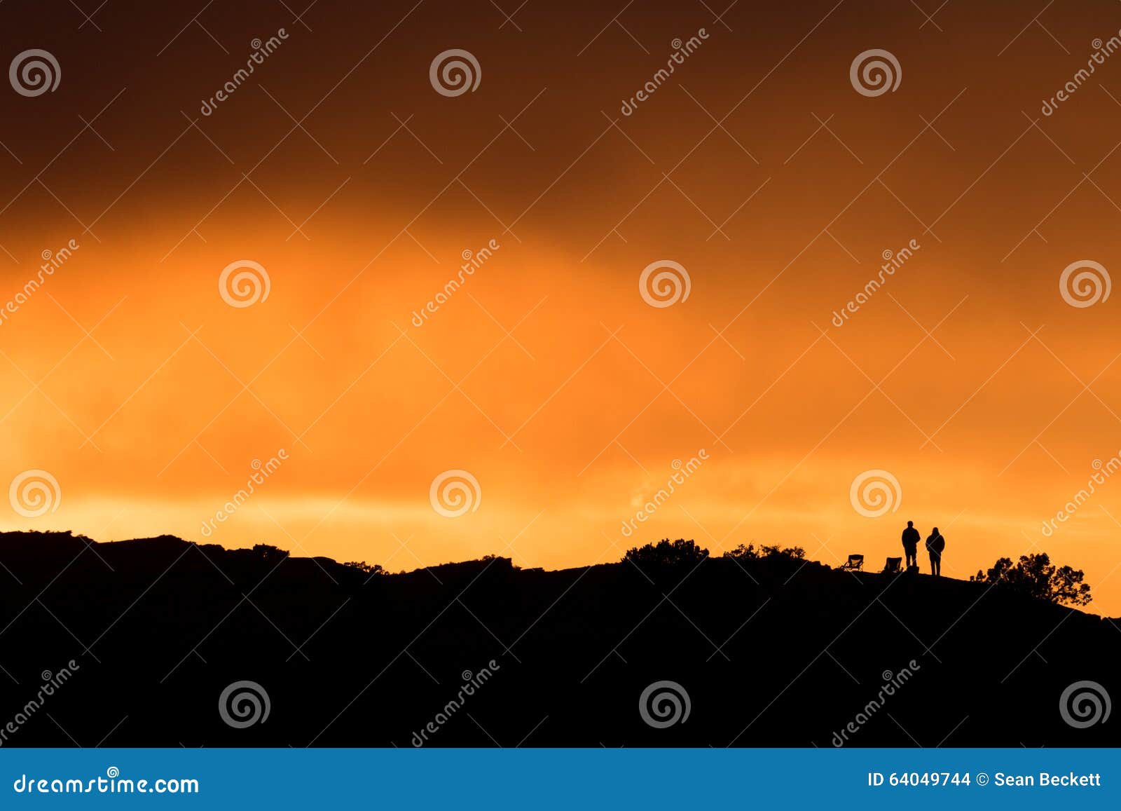 two spectators standing on a hilltop watching sunset