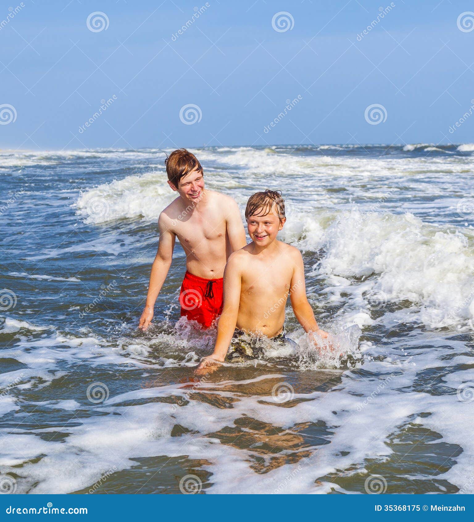 Two teen boys and brothers enjoy the waves in the rough ocean. Boys having fun in the beautiful clear sea
