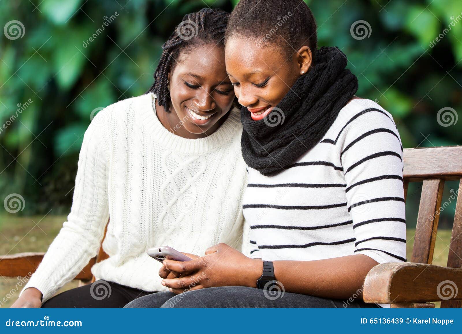 two teenage african girlfriends socializing on phone.