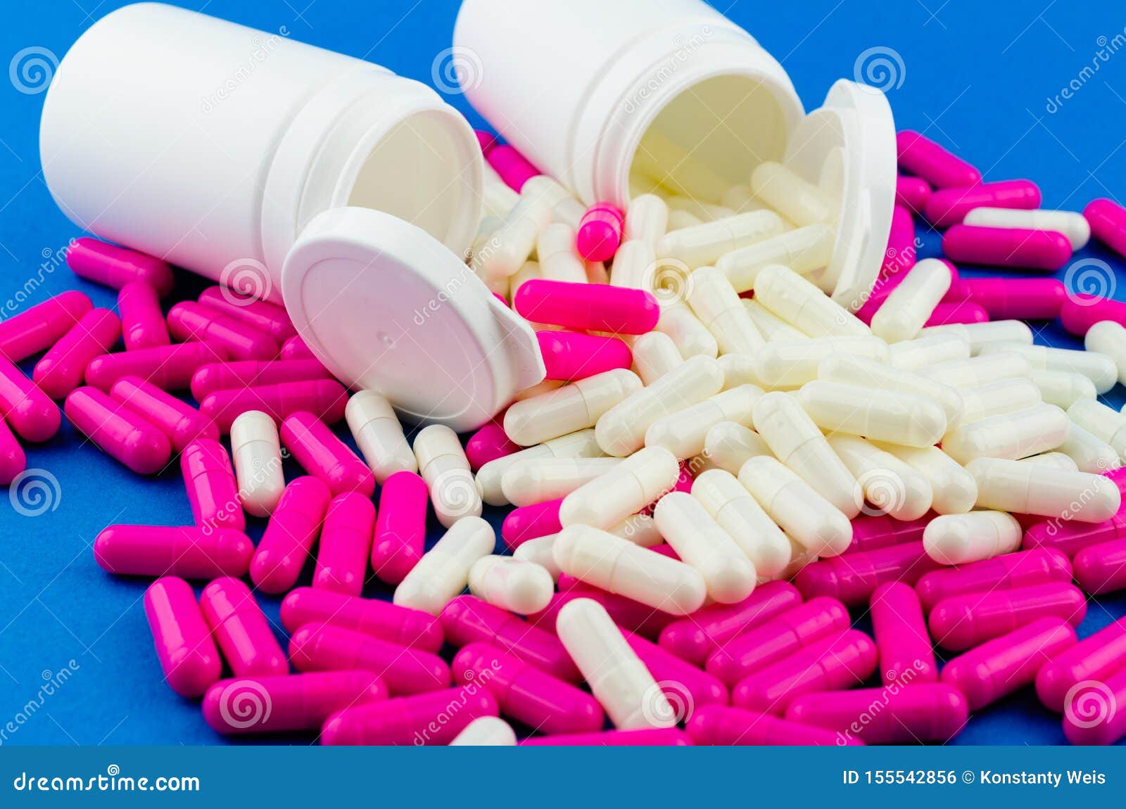 Two White Pill Jars and Scattered Pink and White Capsules on Blue