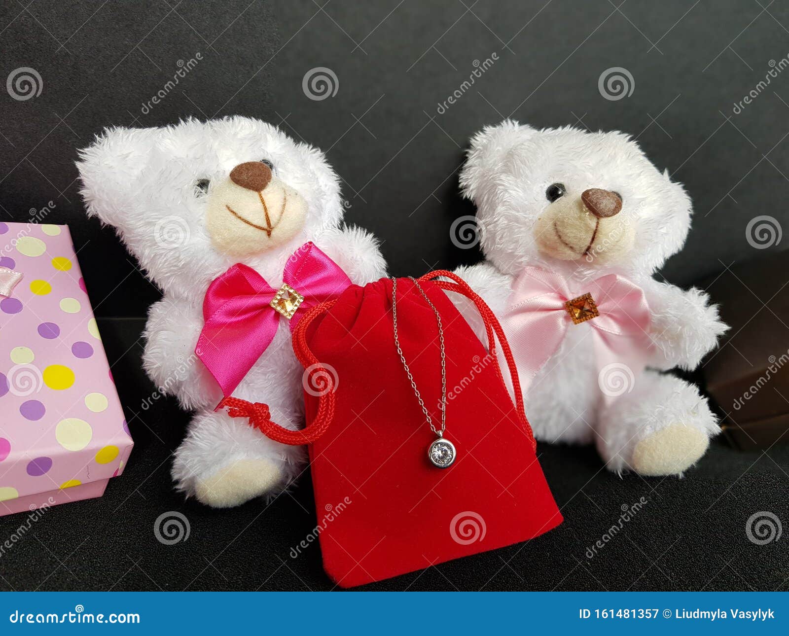 Two White Teddy Bears with a Red Gift Bag and a Pendant on a Chain on a